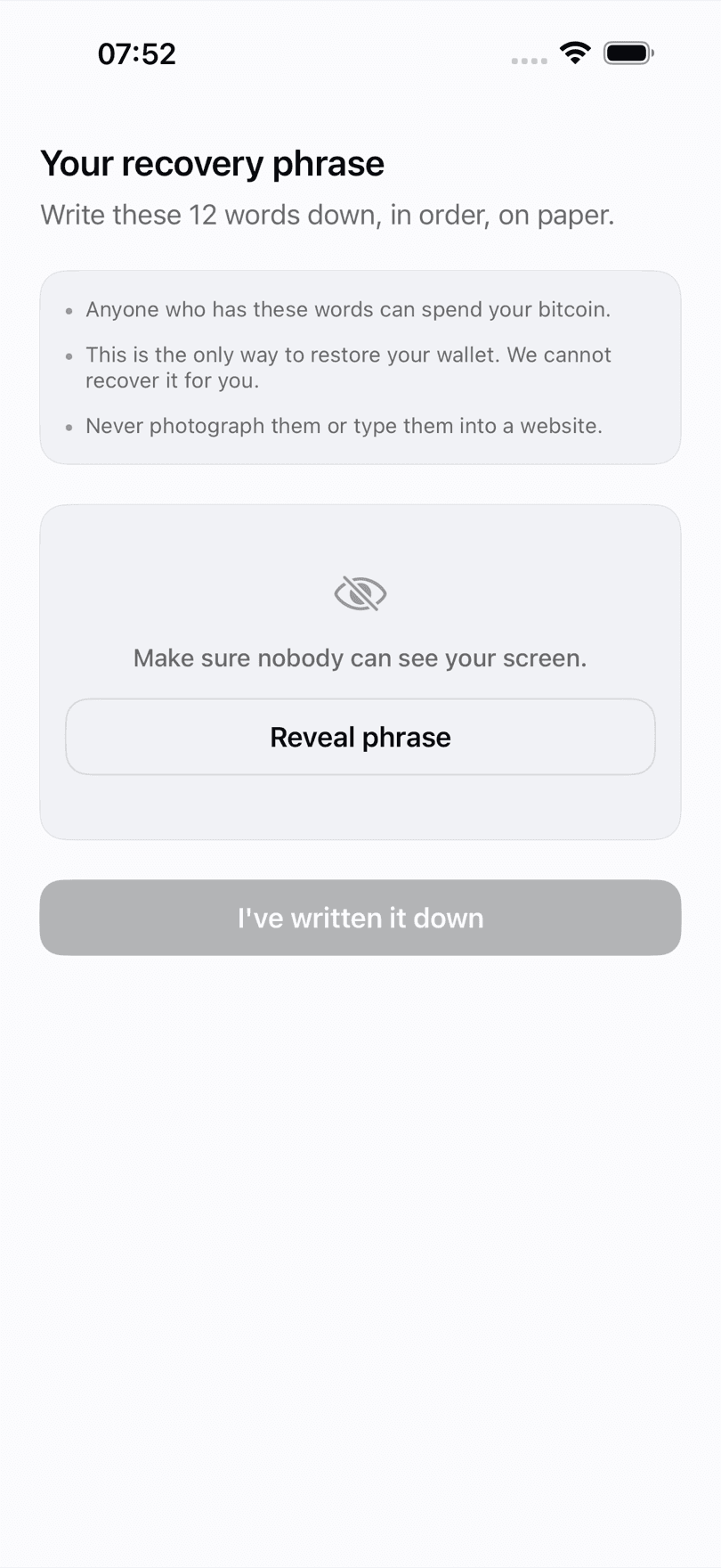 BTC Wallet recovery phrase screen on iPhone, the 12 words still hidden behind a Reveal phrase button, warning that anyone holding them can spend your bitcoin